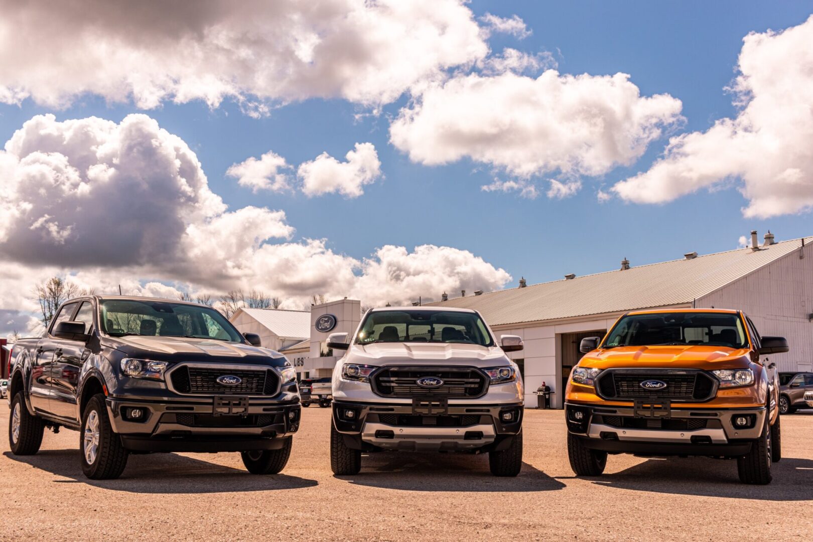Three different trucks parked in a row under some clouds.